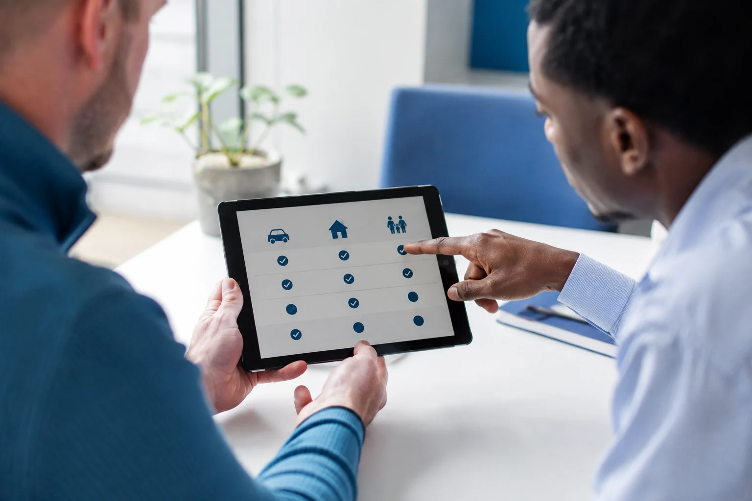 Close-up of hands reviewing a simple insurance coverage comparison on a tablet while another person points to options