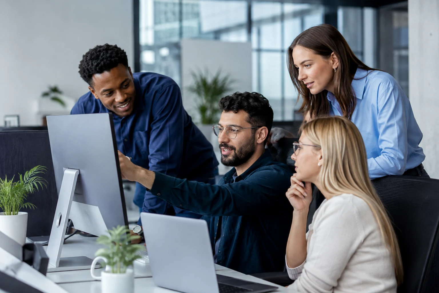 Small modern insurance team collaborating around a large monitor and laptop in an open-plan office